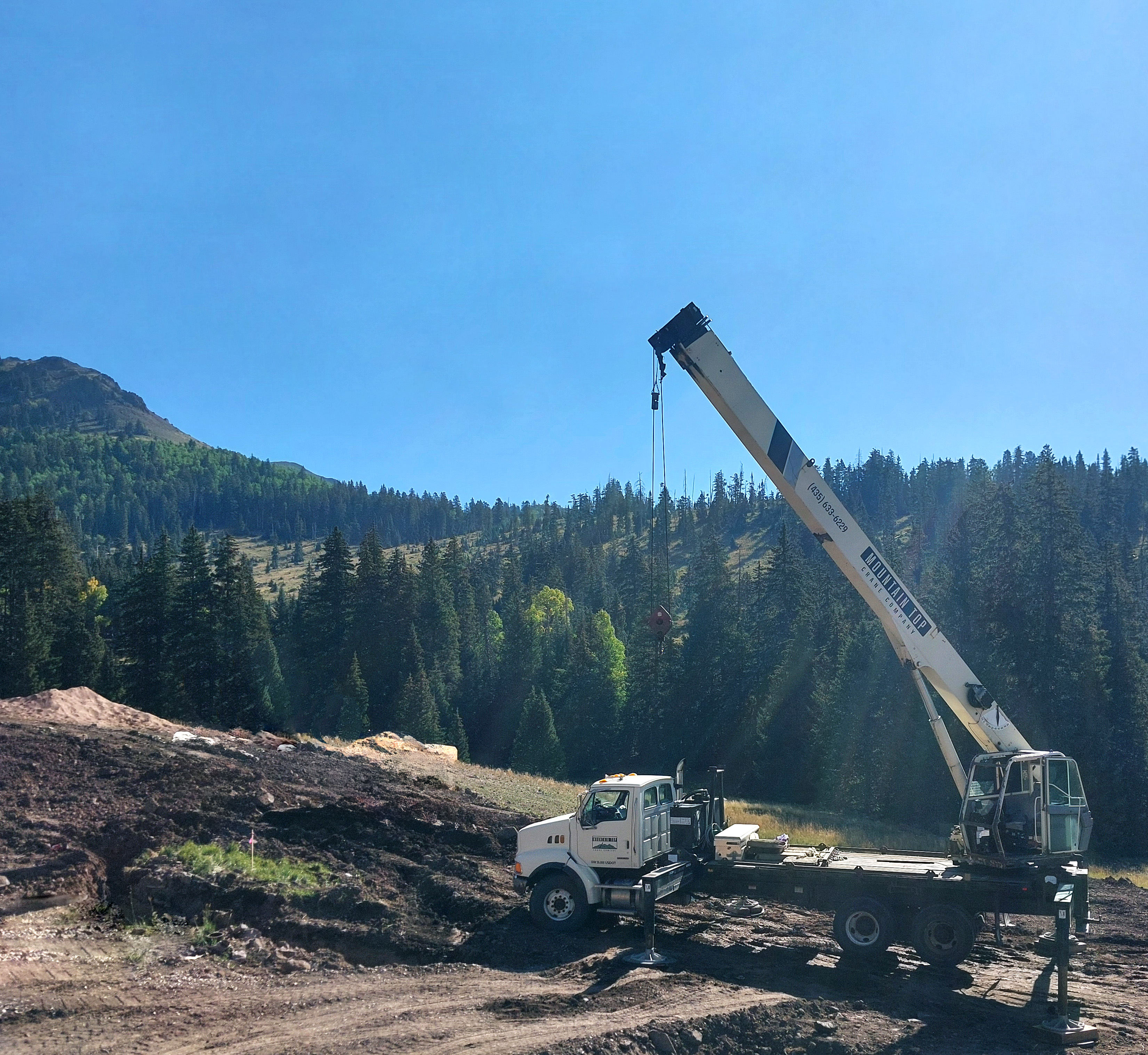 Crane truck parked on alpine mountainside with boom extended above the tree line